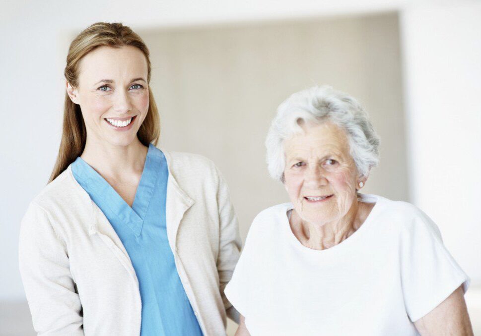 A friendly young medical caregiver standing next to an old lady